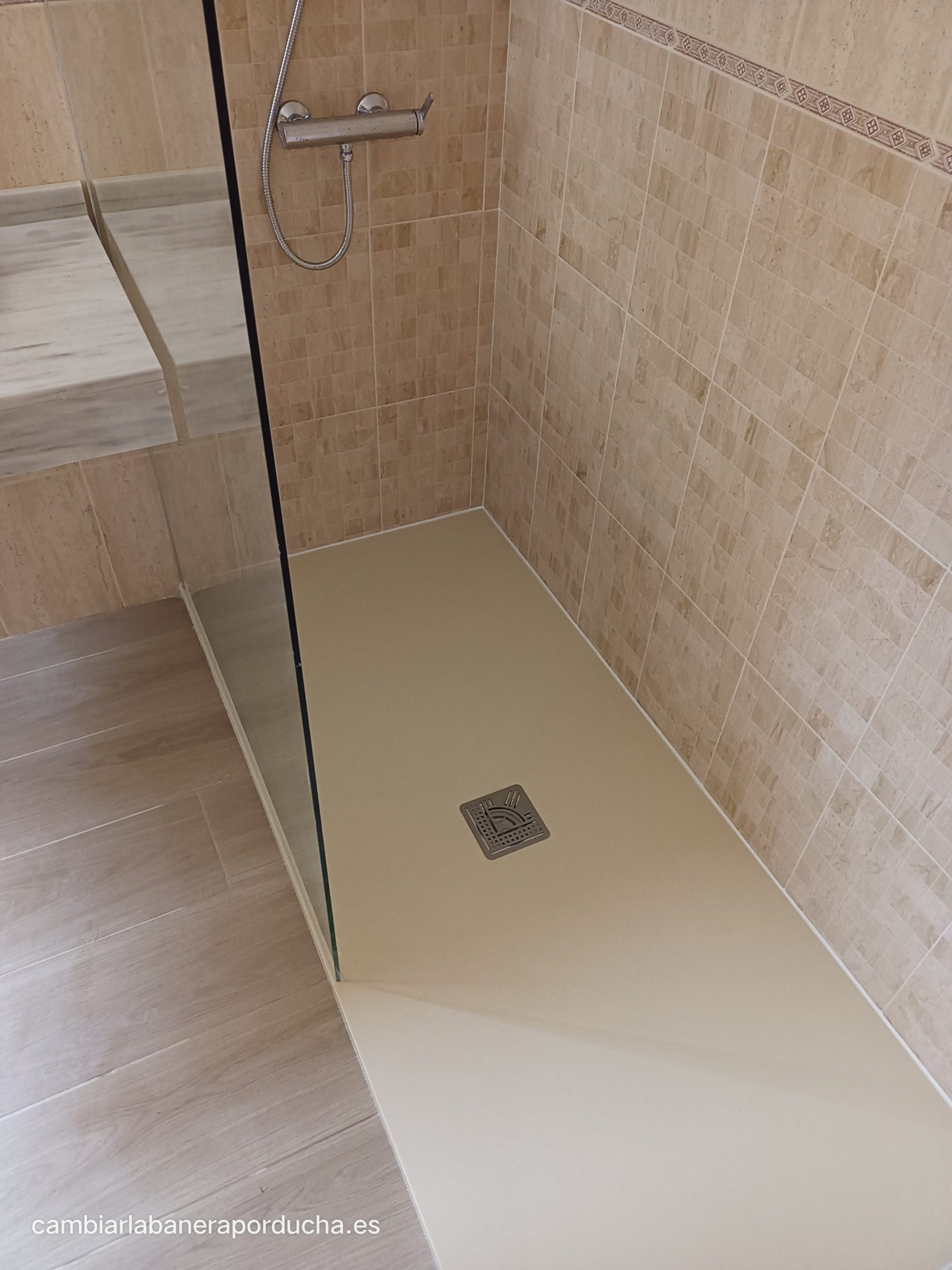 Un plato de ducha de mármol beige se destaca en la imagen, acompañado por un panel fijo de vidrio de 1 metro. Los azulejos del mosaico en tonos beige completan el diseño, brindando un aspecto elegante y sofisticado al espacio.