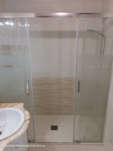 Baño moderno con plato de mármol, mampara frontal de vidrio con 2 paneles fijos y 2 correderos, y azulejos beige a rayas. Estilo elegante y contemporáneo.