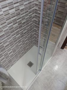 Cambio de bañera con plato de ducha de mármol técnico en blanco Cambio de bañera en Miranda De Ebro. Plato de ducha en color blanco de 120X70 cm. Mampara 1 fijo + 1 corredera + lateral fijo transparete, sin perfil inferior y con tratamiento antical. Azulejo tipo mosaico en color gris en las 2 paredes de la ducha hasta el techo. Desplazar y subir las tomas del grifo a 1 metro