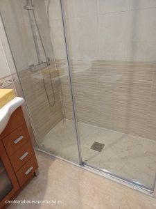 Esta es una foto de una ducha en un baño de Logroño. La mampara está hecha de vidrio y tiene una puerta corredera. Está en la esquina del baño y tiene una alcachofa de ducha y un desagüe en el suelo. El baño tiene azulejos beige en las paredes y el suelo.