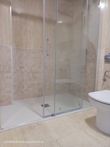 La imagen que me has enviado muestra un baño moderno con una ducha, un lavabo y un inodoro. La foto está tomada desde el interior del baño, con la ducha a la izquierda, el lavabo al centro y el inodoro a la derecha.