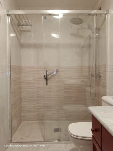 Cambio de bañera por ducha en Fuenmayor, La Rioja. La imagen muestra un plato de ducha de resina blanco con textura antideslizante y un diseño moderno, junto a una mampara de ducha de cristal templado transparente y perfilería de aluminio. Los azulejos beige en las paredes y el toallero negro completan el look moderno y elegante del baño.