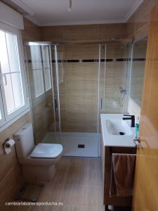 Esta imagen muestra una renovación de baño en la localidad de Oyón, La Rioja.Se ha realizado un cambio de plato de ducha por otro plato.La ducha es amplia y a ras de suelo. Está cerrada con puertas de vidrio transparente y cuenta con acabados modernos. El plato de ducha es de color blanco y está equipado con grifos cromados.