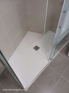 Esta imagen muestra un cambio de bañera a medida por plato de ducha realizado en un baño en Tirgo (La Rioja). La reforma ha dado como resultado un baño elegante, funcional y con un aprovechamiento óptimo del espacio, gracias al plato de ducha de mármol carrara a medida que se adapta perfectamente a la forma del baño. El plato de ducha se complementa con un grifo termostático, kit de ducha y mampara de vidrio serigrafiado. Los azulejos del baño son de color gris y están colocados hasta el techo, lo que crea una sensación de amplitud