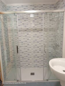 Esta imagen muestra un cambio de bañera por ducha realizado en un baño en Logroño. La reforma ha dado como resultado un baño moderno, elegante y funcional, con un plato de ducha de mármol blanco, azulejos tipo mosaico en color azul en las tres paredes hasta el techo, mampara de 2 paneles fijos y 2 paneles correderos, grifo termostático y barra fija para regular el rociador en altura. Esta reforma es una excelente opción para aquellos que buscan un baño práctico, estético y que aproveche al máximo el espacio disponible.