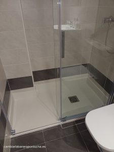 "Reforma de baño en Tudela (Navarra): Plato de ducha extraplano con rodapié de mármol técnico, azulejos de gran formato y mampara de cristal transparente. Diseño moderno y minimalista para un baño cómodo y funcional.