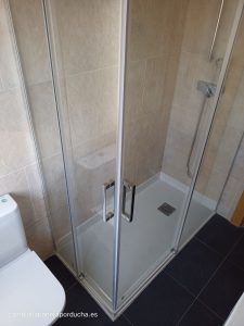 Baño reformado en Miranda de Ebro con un nuevo plato de ducha rectangular, paredes de azulejos en tonos beige, mampara de cristal con puertas correderas y detalles cromados.