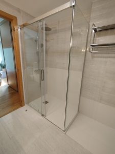 Cambio de bañera por ducha en Sarriguren (Pamplona). Baño moderno con plato de ducha extraplano blanco, mampara de cristal con perfilería cromada y paredes revestidas con placas de mármol técnico en color blanco, logrando un acabado amplio, luminoso y elegante.