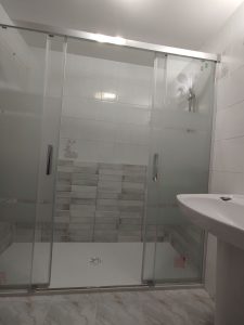 Reforma de baño en Cuzcurrita: cambio de bañera por ducha con plato blanco y frente de azulejo decorativo.