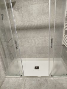 Cambio de plato de ducha por plato de ducha en Cenicero, La Rioja: instalación de plato blanco de carga mineral con mampara corredera frontal y azulejos grises texturizados.